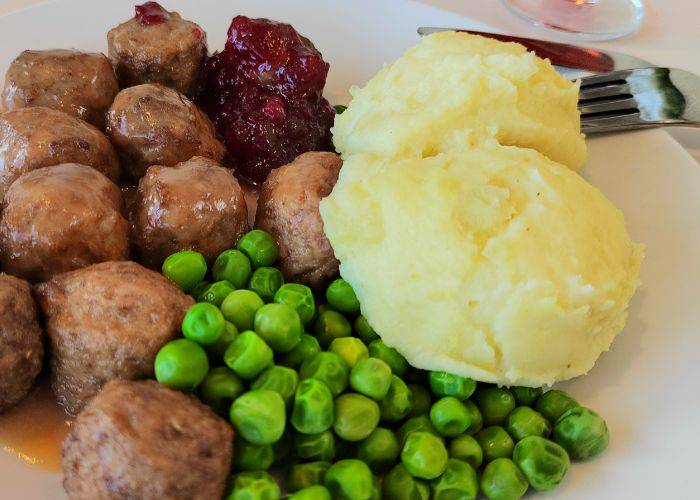 A close-up of IKEA's Swedish meatballs, served with peas, mashed potato,, cranberry sauce and gravy.